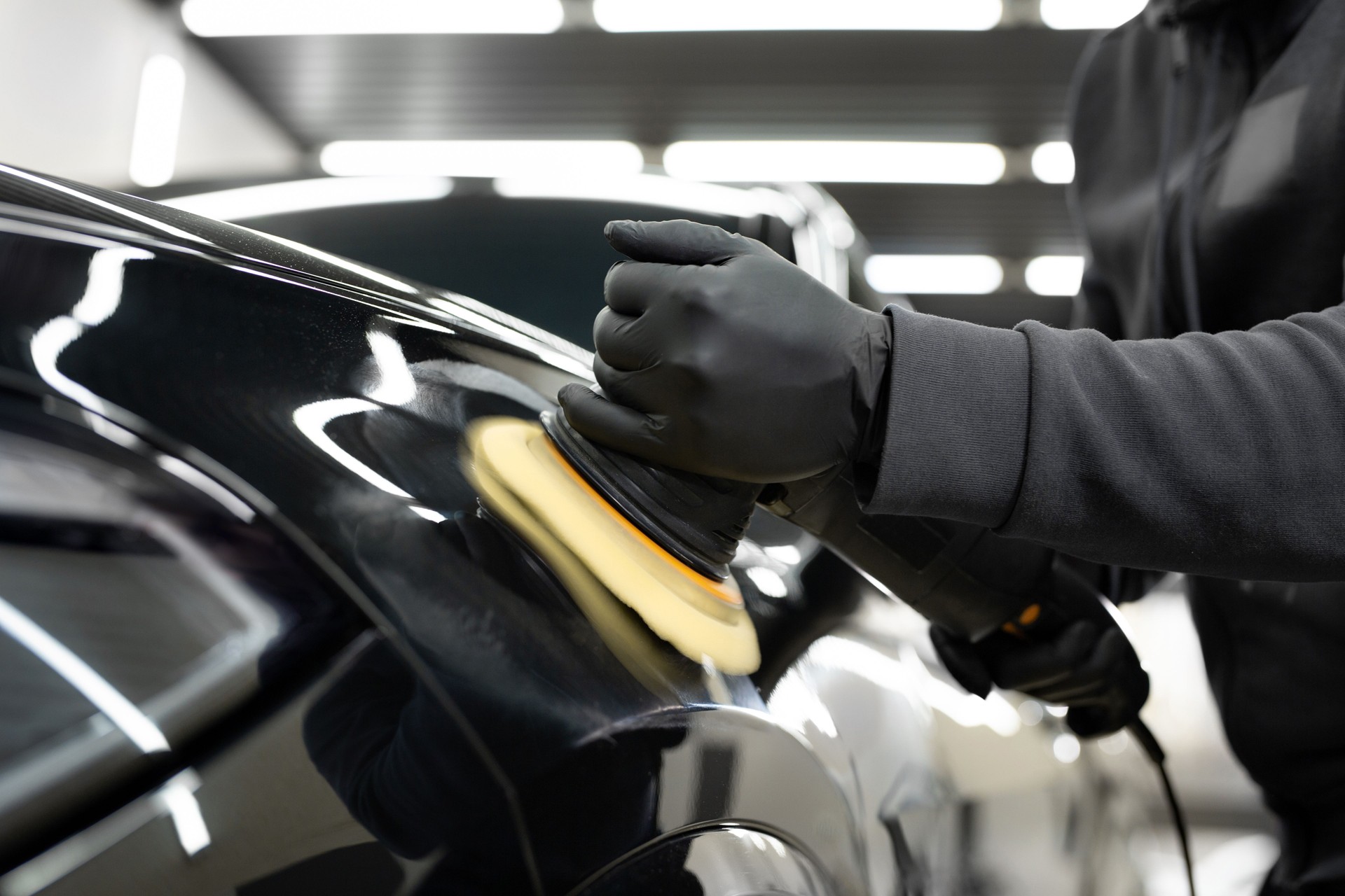 Professional detailing a car in car studio, hands with orbital polisher, scratching remover, vehicle care concept.
